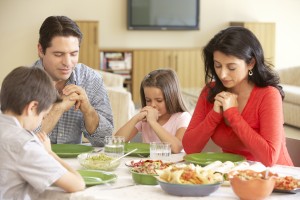 Young Hispanic Family Saying Prayers Before Meal At Home